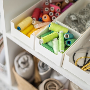A close-up view shows several small white organization bins filled with colorful thread, tape measures, and sewing scissors.