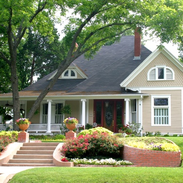 A light brown residential house features a brick stair walkway leading to the front door and a garden with flowers.