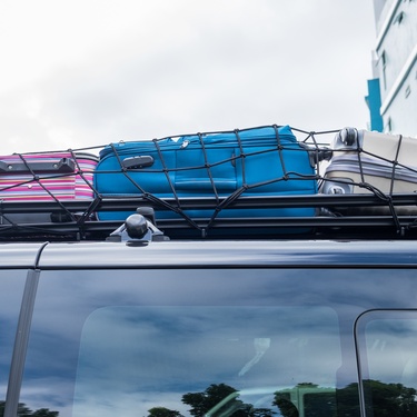 A stretchy black cargo net secures three suitcases in the roof rack of a black vehicle.