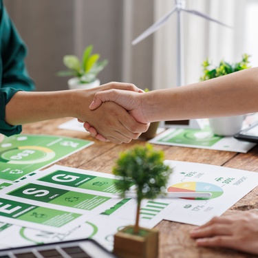 A close-up of businesspeople shaking hands, above a green finance document during an ESG strategy workshop.