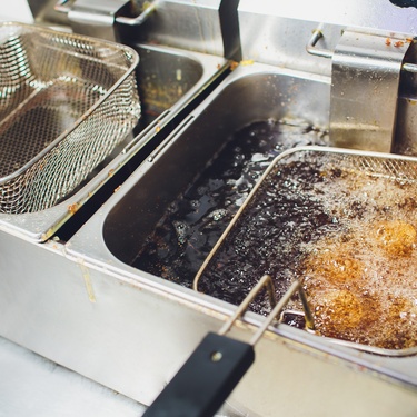 A commercial deep fryer with two baskets. One of the baskets is submerged in bubbling oil.
