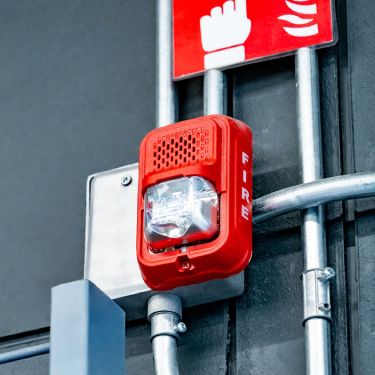 A red fire alarm system sits on a wall with the word 'FIRE' on it. Multiple metal pipes connect to the system.