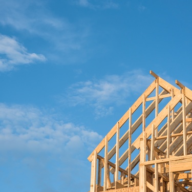The upper level and roof of an unfinished home with only wooden trusses, posts, and beams against a clear blue sky.