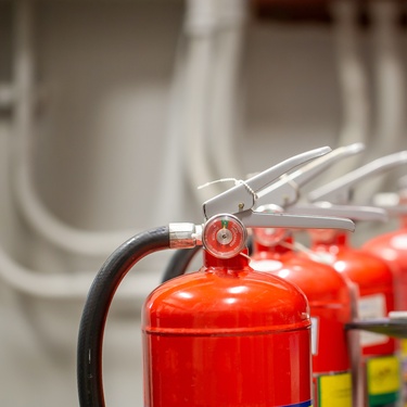 A person is standing next to a line of fire extinguishers. The person is holding a clipboard.