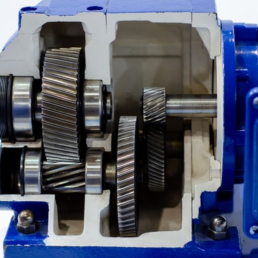 A blue industrial gearbox with exposed helical gears and shafts with a sectional view its internal mechanical components.