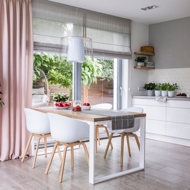 A Bright modern dining area with white chairs and wooden table beside large window and indoor plants.