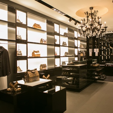 A retail store highlights its handbag and clothing products using backlights. There is a black chandelier in the middle.