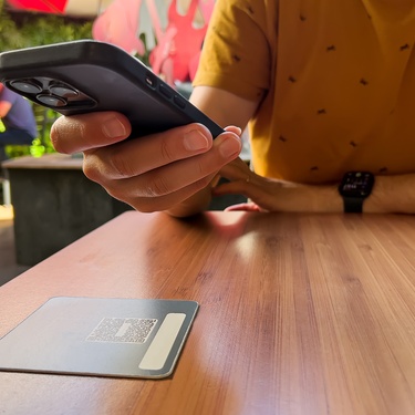 A close-up of a person scanning a QR code with their phone at a restaurant, with the code placed on a wooden table.
