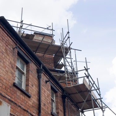 A close-up of the roofline of an older red brick building currently being renovated or repaired, with extensive scaffolding.