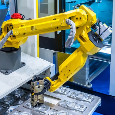 The yellow robot arm of a CNC machine is carving multiple pieces of metal that all look the same.