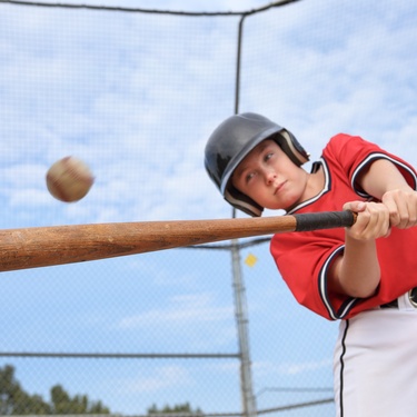 A young boy wearing a black helmet, a red shirt, and white pants is hitting a baseball with a wooden baseball bat.