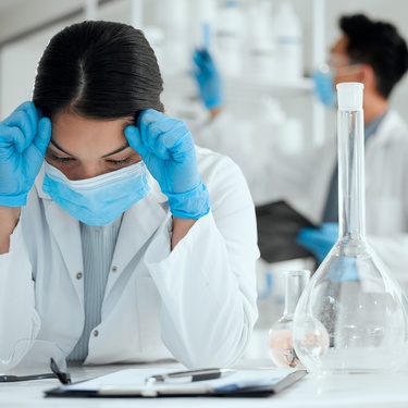 A woman scientist is experiencing burnout in a laboratory for medical research. She's showing a stressed facial expression.