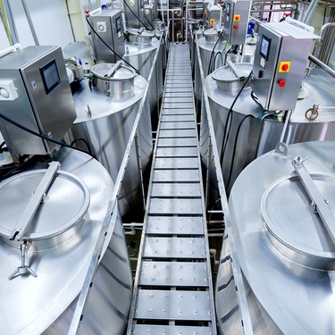 A room with large, metallic structures. There is a conveyor belt between the structures and various tubes connecting to the structures.