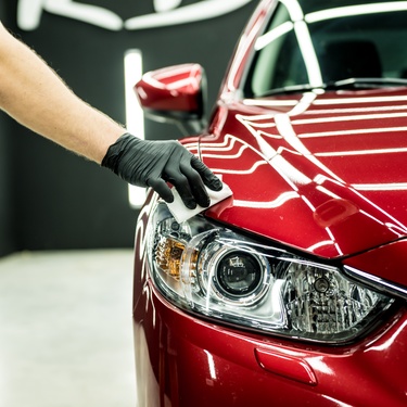 A close-up of someone's arm and gloved hand wiping off a red-painted car. The car is shiny and clean.