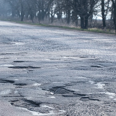 A clear road with multiple potholes that can damage a vehicle. In the distance, a car is approaching.