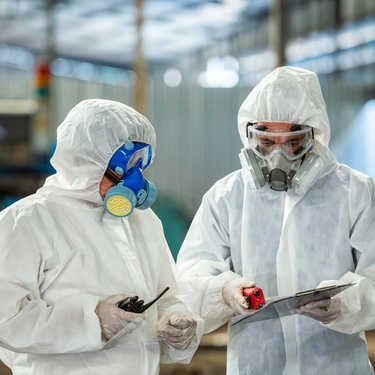 Two employees in white personal protective equipment hold walkie-talkies while reviewing a clipboard.