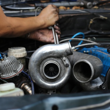A man holds a wrench to the inside of a vehicle engine, with the turbocharger in the forefront.