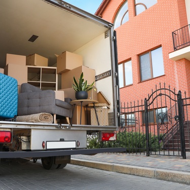 A moving truck full of boxes and furniture parked outside of a house with a black, wrought-iron fence.