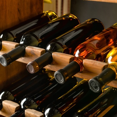 A wine rack, up close, with ten unlabeled bottles stored horizontally on it in a dimly lit indoor area.