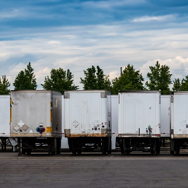 A bunch of white semi-truck trailers parked next to each other. Some are parked vertically, while others are horizontal.