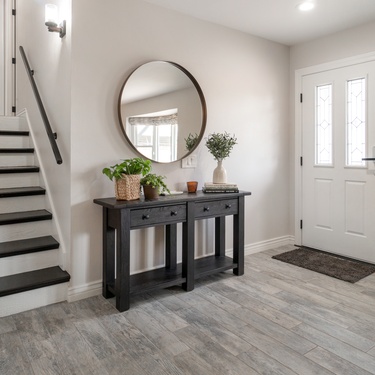 A home entryway with a white front door and a round mirror on the wall. A small staircase leading upstairs is nearby.