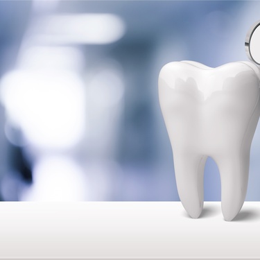 A model of a tooth and a dentist's mirror standing upright next to each other on a white table in a harshly lit room.