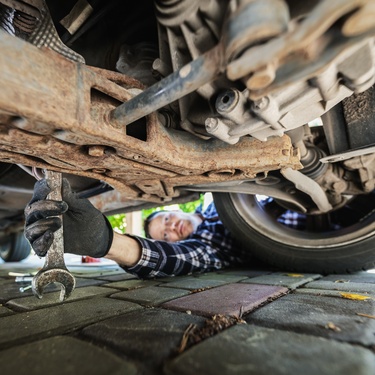A person wearing black gloves and holding a wrench. They are using the wrench to work on the underside of their car.