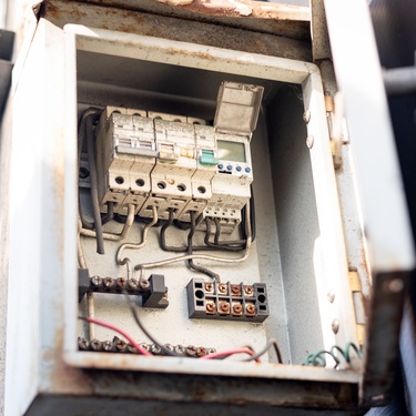 An open white electrical box with components covered in a layer of dust. Several cables connect each part.