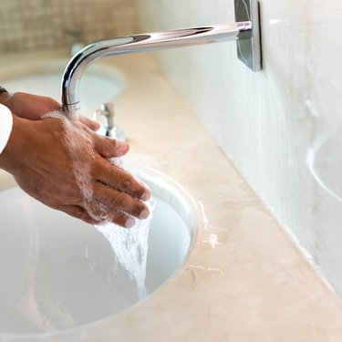 A person reaching beneath an active silver faucet to rinse their hands. The water runs into a deep sink.