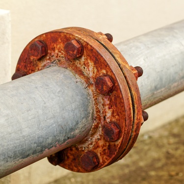 Two steel pipes connected with bolts in the center, where a red ring of rust or corrosion has formed.