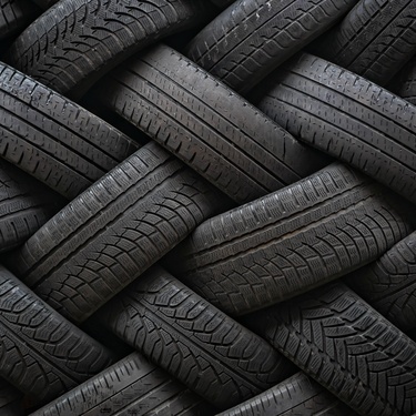 A close-up of various tires woven into a pile. There are different treads, and some tires are more worn than others.