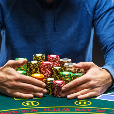 An individual in a blue shirt hovers over a large stack of colorful poker chips on a green felt table.