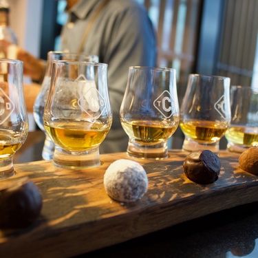 Five sleek nosing glasses with custom-engraved logos are lined up on a table. They all have whiskey poured into them.