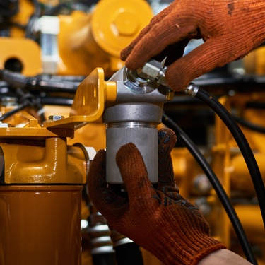 A person with red gloves on, adjusting a component of an industrial hydraulic system. Most of the machinery is yellow.