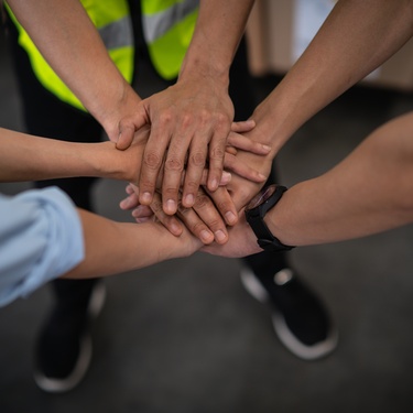 A few people putting their hands together to symbolize teamwork. Each person has both of their hands in the stack.