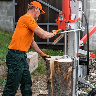 A man working with a log splitter outside. He's wearing a bright yellow shirt and hat with black pants on.