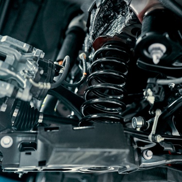 A close-up of the rear suspension of a car. Every component looks shiny and new with a large spring in the middle.