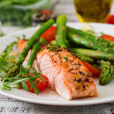 A healthy dinner plated with a piece of seasoned fish, asparagus, and greens on the side as garnish.