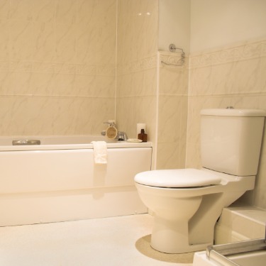 A neutral builder-grade bathroom with beige tile, a white bathtub, a pedestal sink, and a toilet.