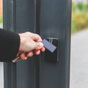 A close-up shows a person holding an electronic access fob to a mounted reader. Metal keys are attached to the fob.