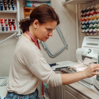 A woman adjusting a computerized embroidery machine in a sewing workspace with thread spools and tools nearby.