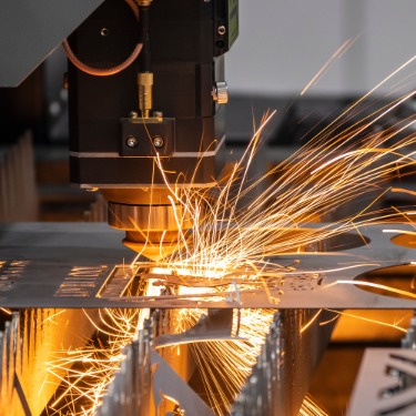 A metal fabrication machine is working on a sheet of metal. Sparks are flying of the metal.