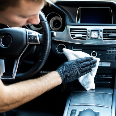 A man wearing black gloves is using a towel to clean the dashboard of a car. The man has short hair.