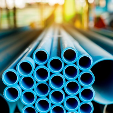 A close-up of the end of a pile of blue plastic PVC pipes. In the pile are many smaller pipes that fit between larger ones.