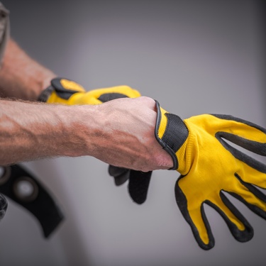 A construction worker pulls on yellow and black work gloves before starting a job site task.