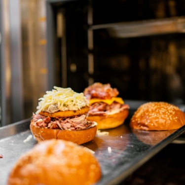 A chef removing a pan containing two toasty sandwiches from a commercial oven in a restaurant kitchen.