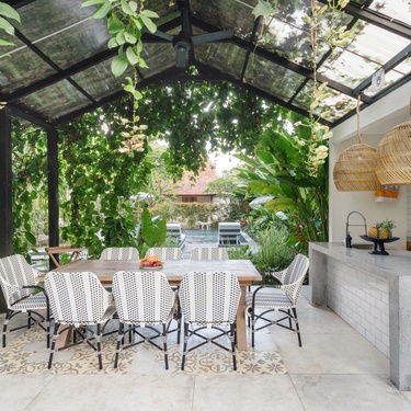 An outdoor kitchen in a residential yard with a full dining area. Green leaves surround the kitchen on a sunny day.