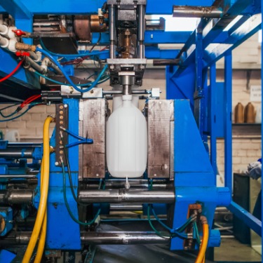A large, white plastic polyethylene canister being manufactured on a massive, light blue automatic conveyor.